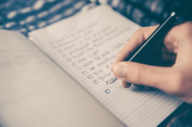 Close-up of a hand with a pen ticking off items in a checklist on grid notebook paper