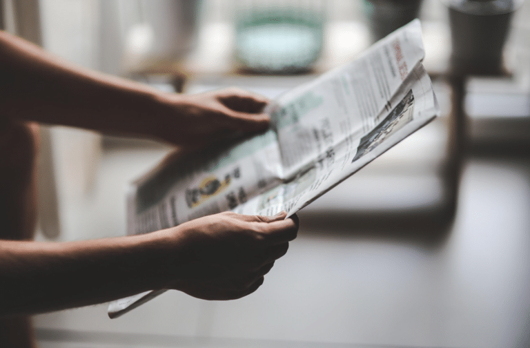 Person holding and reading a folded newspaper indoors with both hands